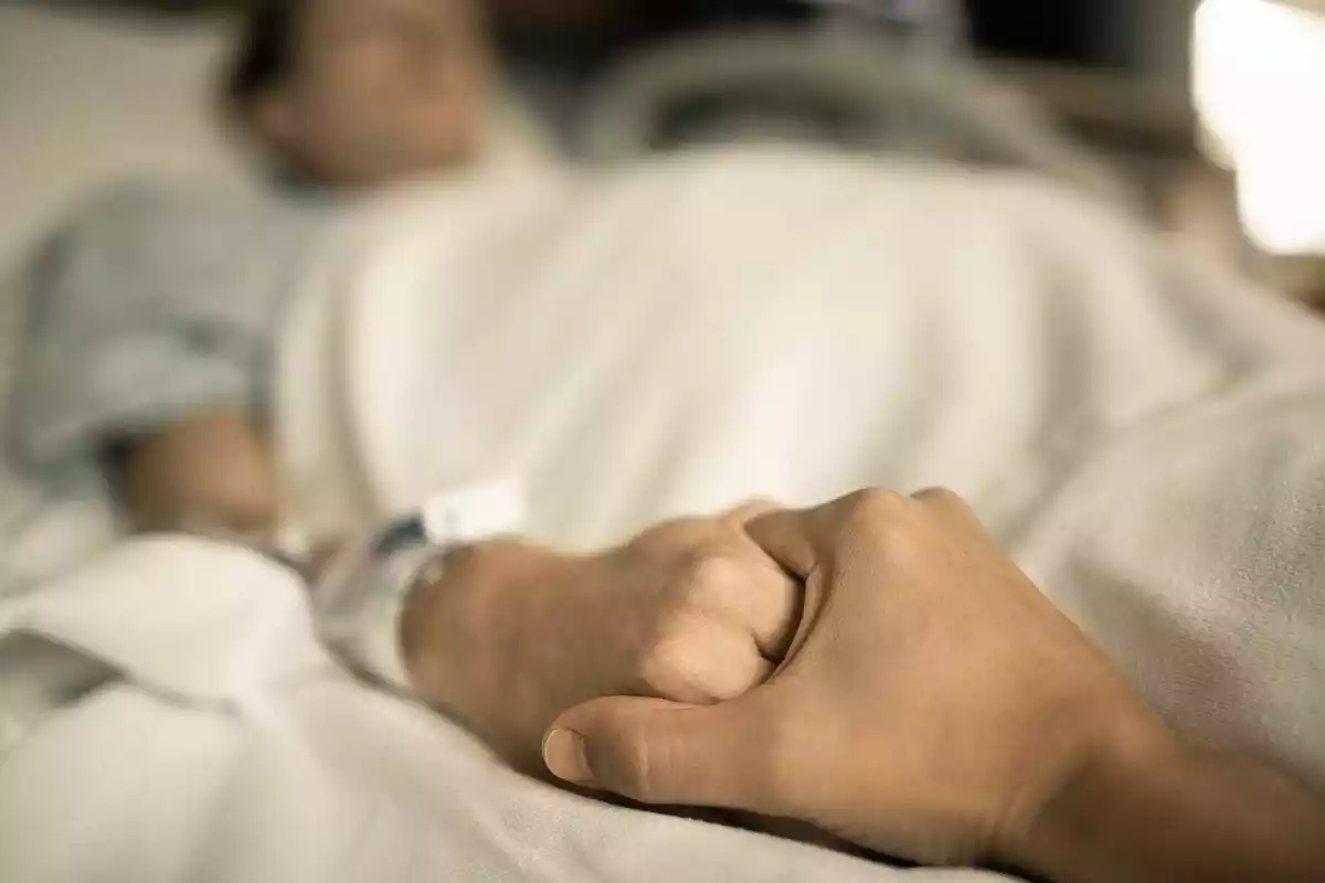 Un home subjecta la mà d'una dona en un llit d'hospital