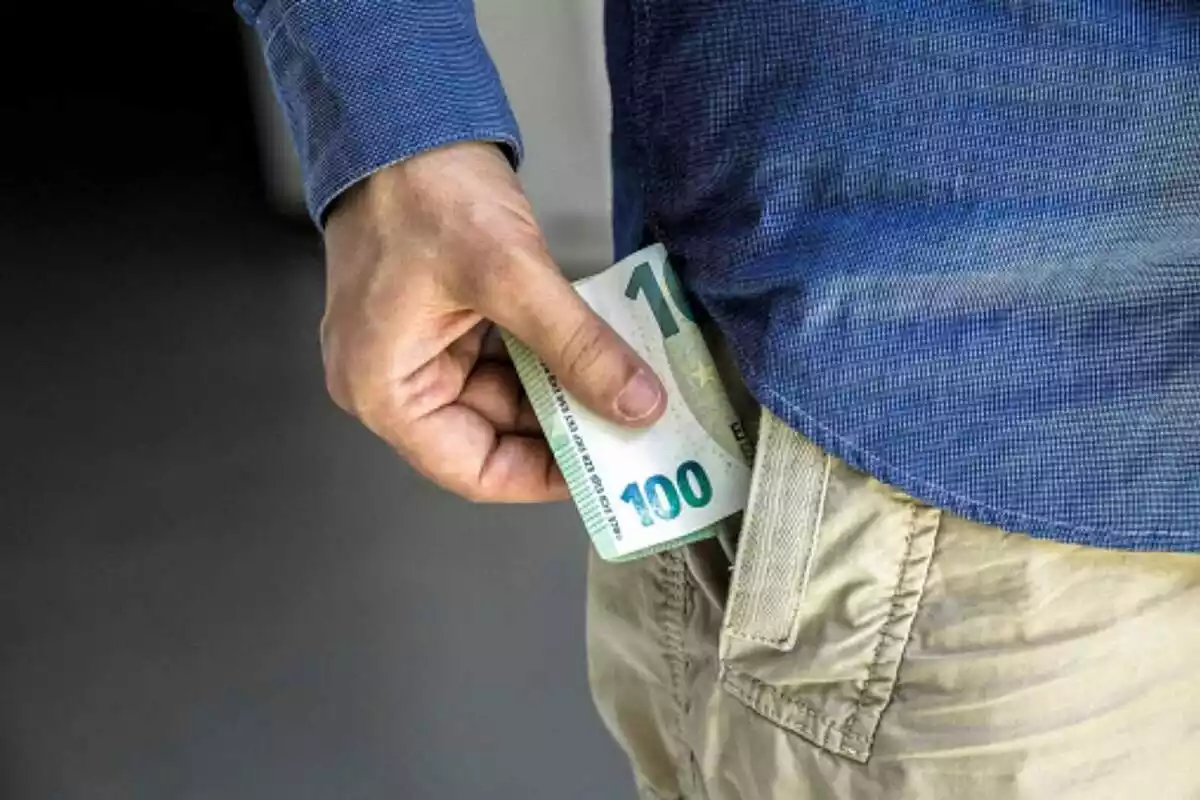 Primer pla de la mà d'un home posant-se un bitllet de 100 euros a la butxaca