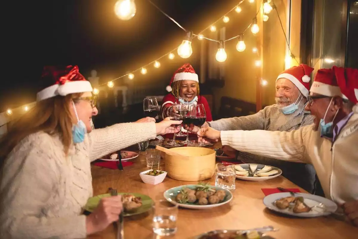 Diverses persones fent un sopar de Nadal amb barrets de Pare Noel i mascareta.