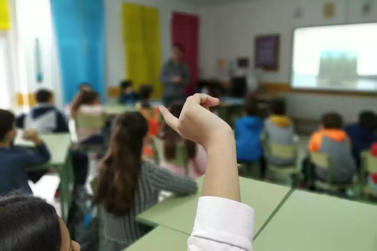 Imatge d'una classe en una escola amb una nena aixecant la mà