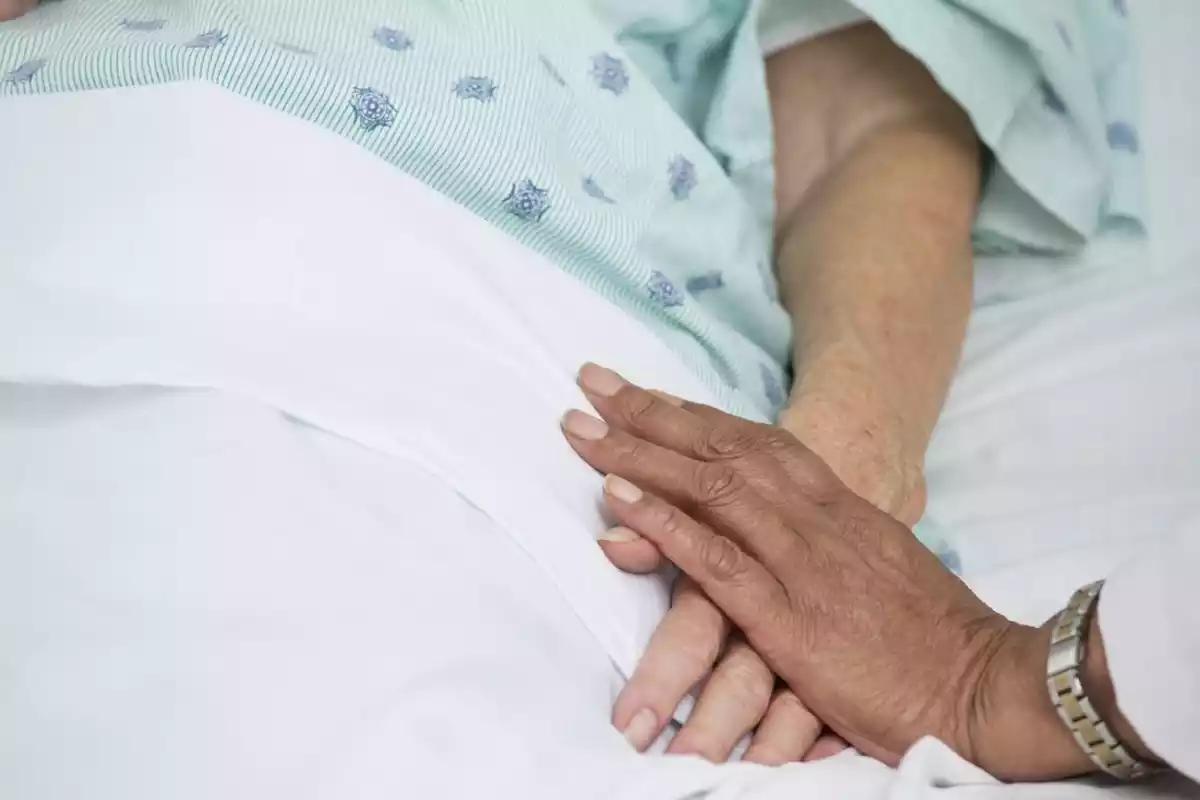 Detall de la mà d'una persona damunt de la d'una dona gran a l'hospital