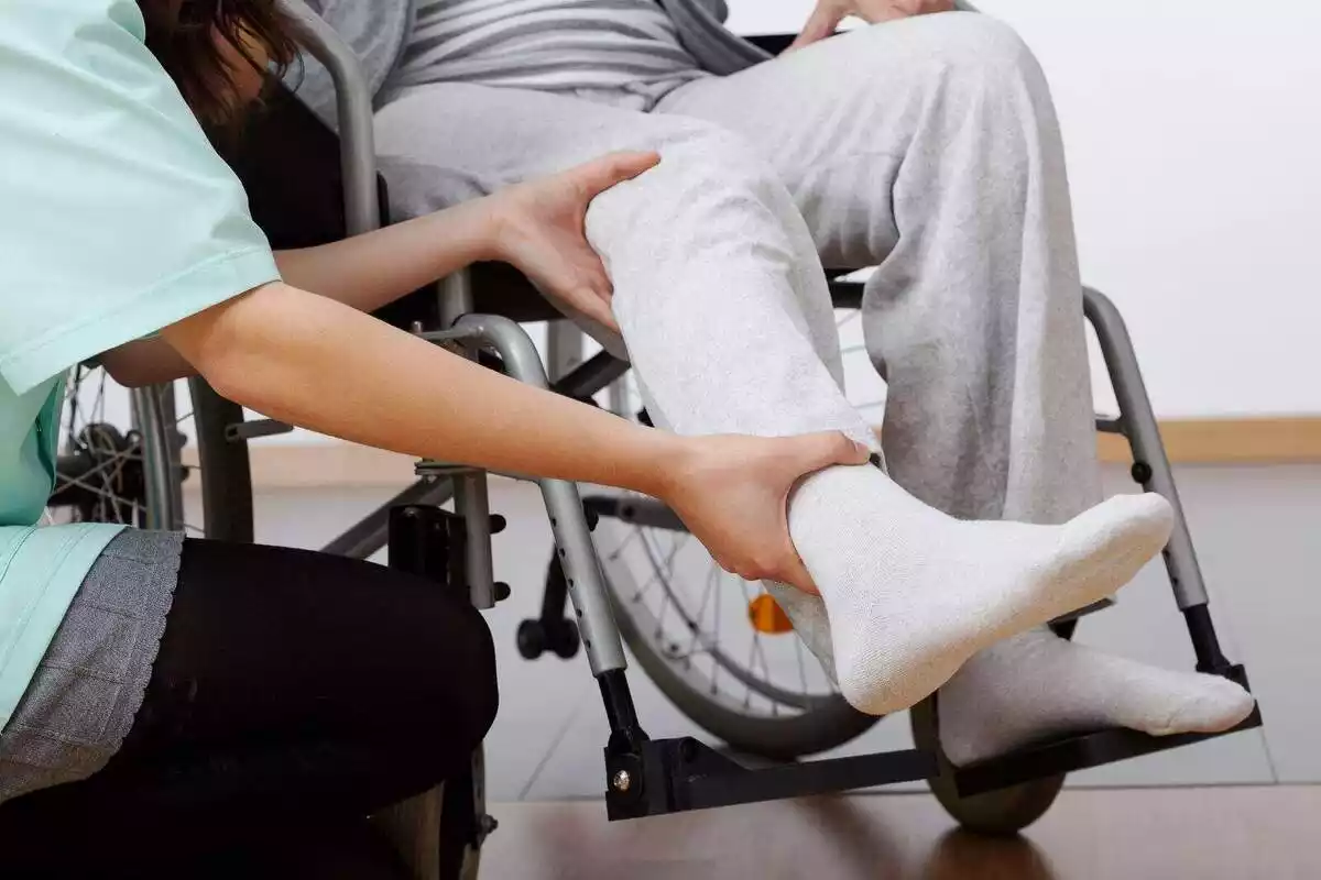 Imatge d'un fisioterapeuta realitzant-li exercicis a un paraplègic en cadira de rodes