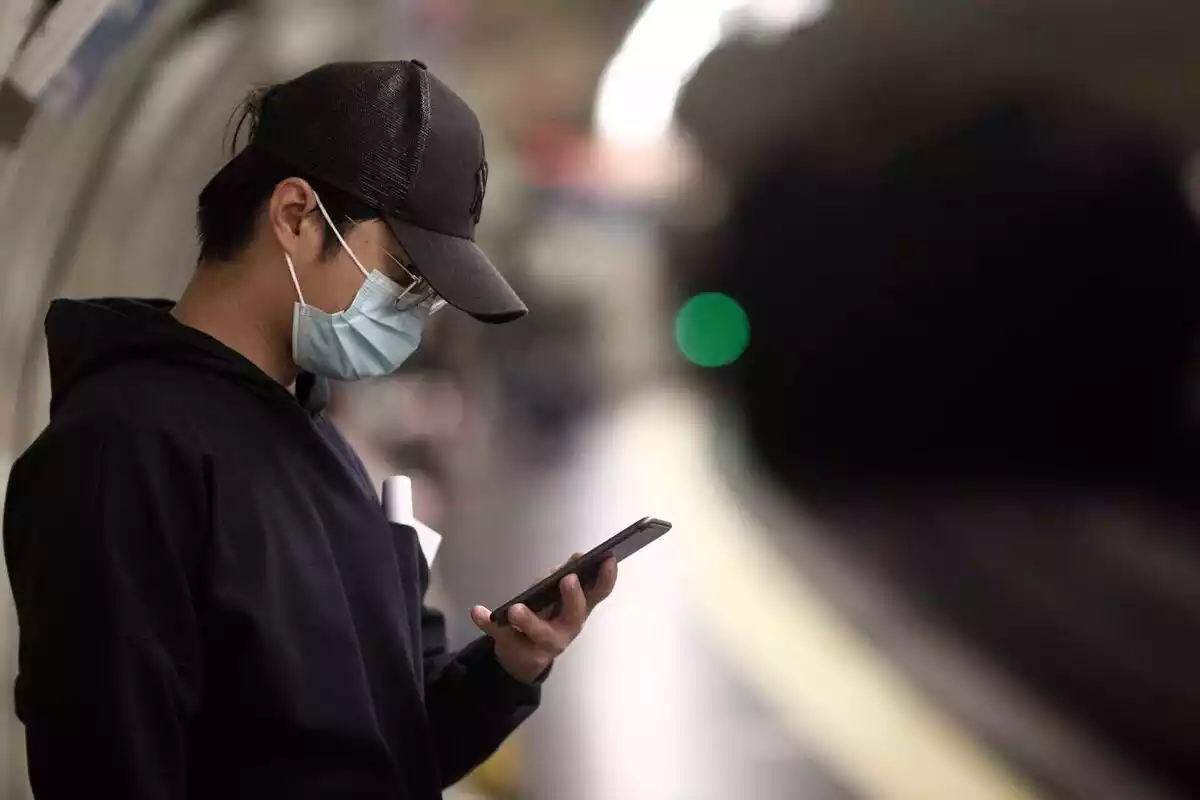 Un noi amb mascareta que mira el mòbil mentre espera el metro.
