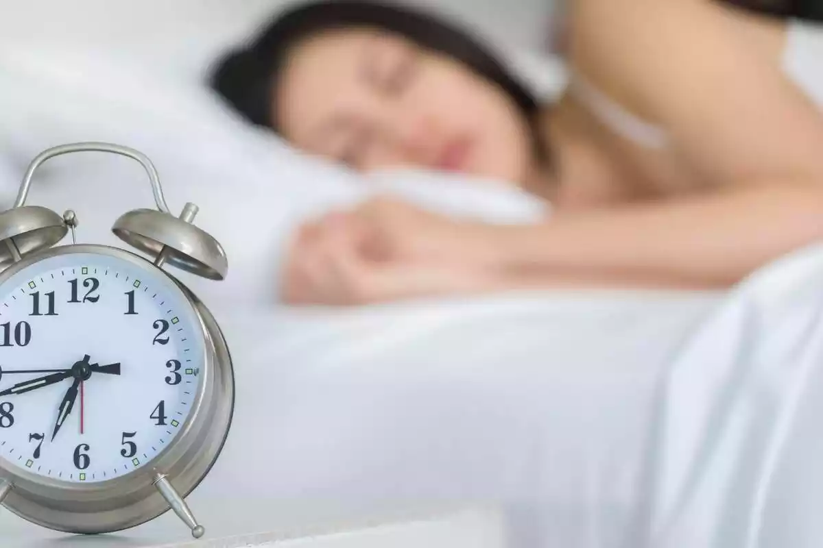 Imatge d'una dona dormint de fons i un despertador