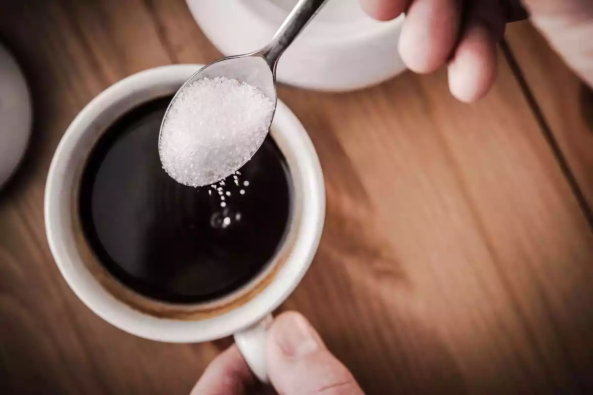 Persona posant sucre al cafè