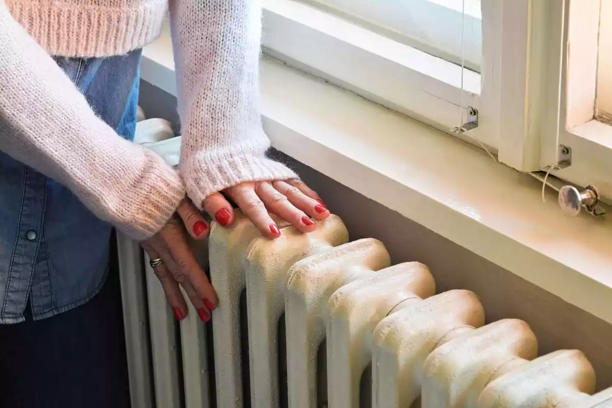 Una dona s'escalfa les mans en un radiador.