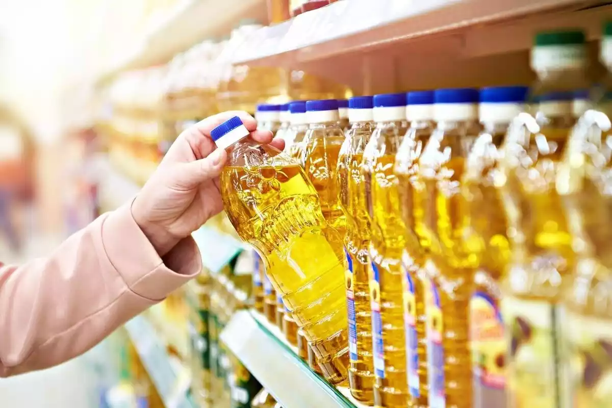 Una dona agafant una botella d'oli d'oliva en un supermercat.