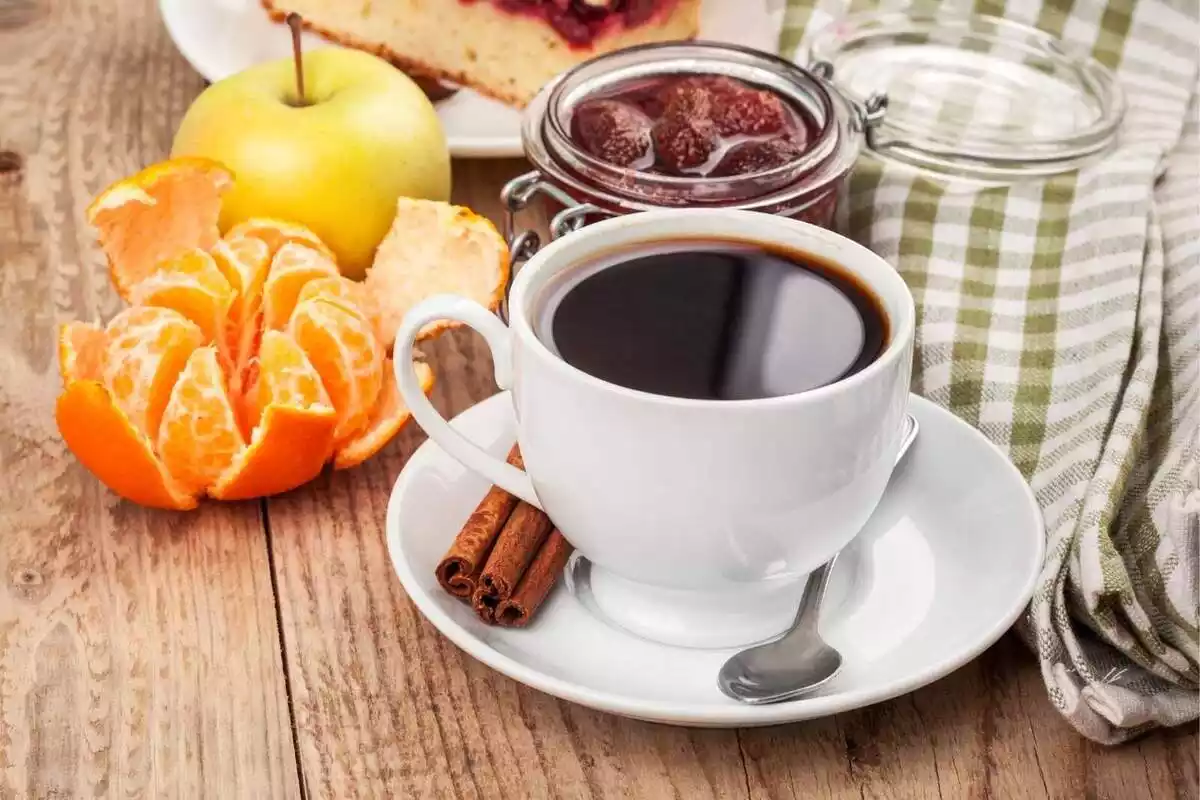 Una tassa de cafè amb fruita i un tros de pastís al costat