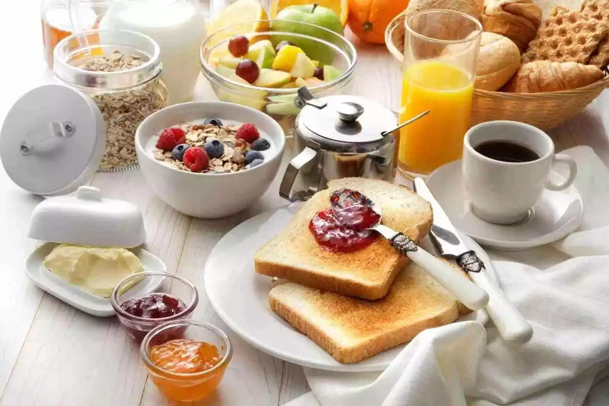 Imatge d'una taula amb diversos aliments com a cereals, suc de taronja, torrades, etc., per esmorzar