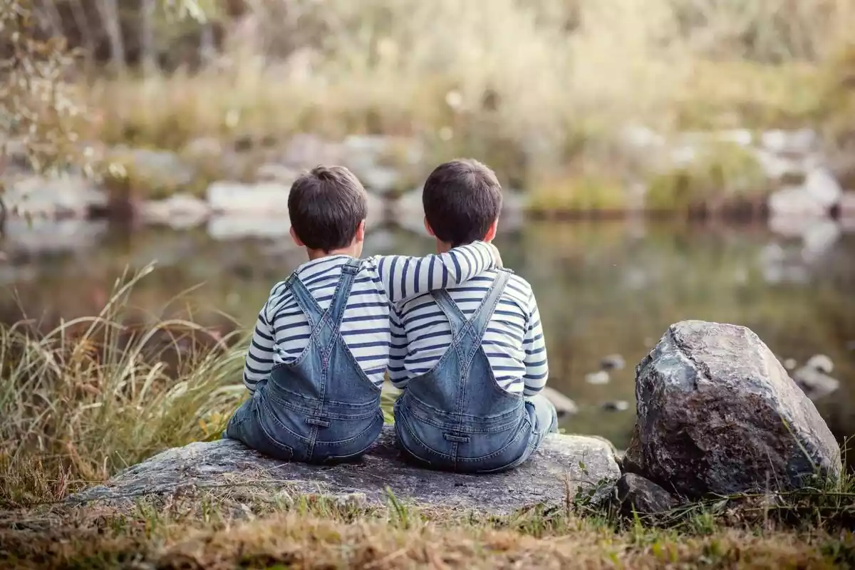 Imatge de 2 germans vestits igual asseguts en una roca i abraçats pel coll