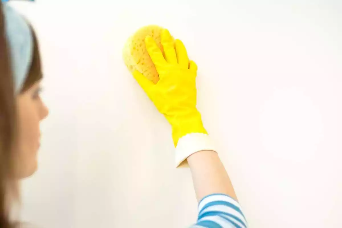 Dona netejant una paret blanca amb guants i esponja