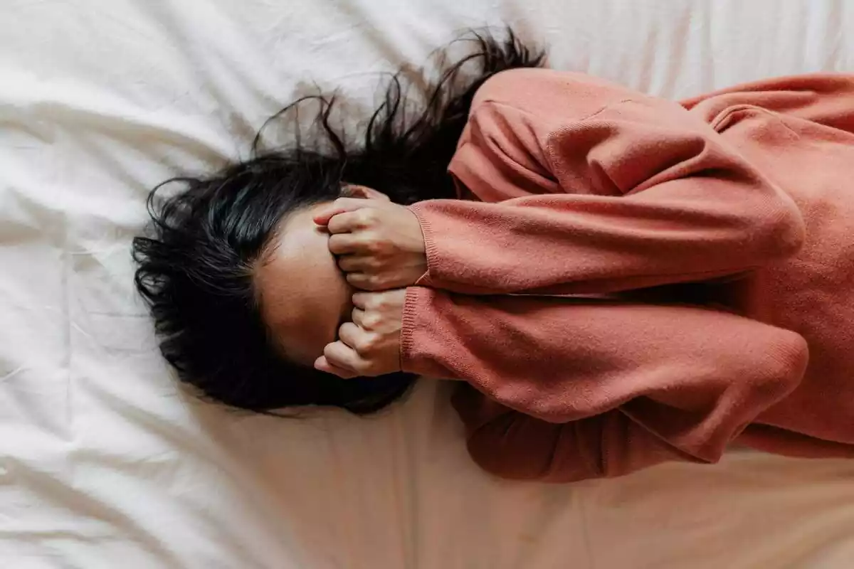 Foto d'una dona estirada al llit i tapant-se els ulls amb les mans.