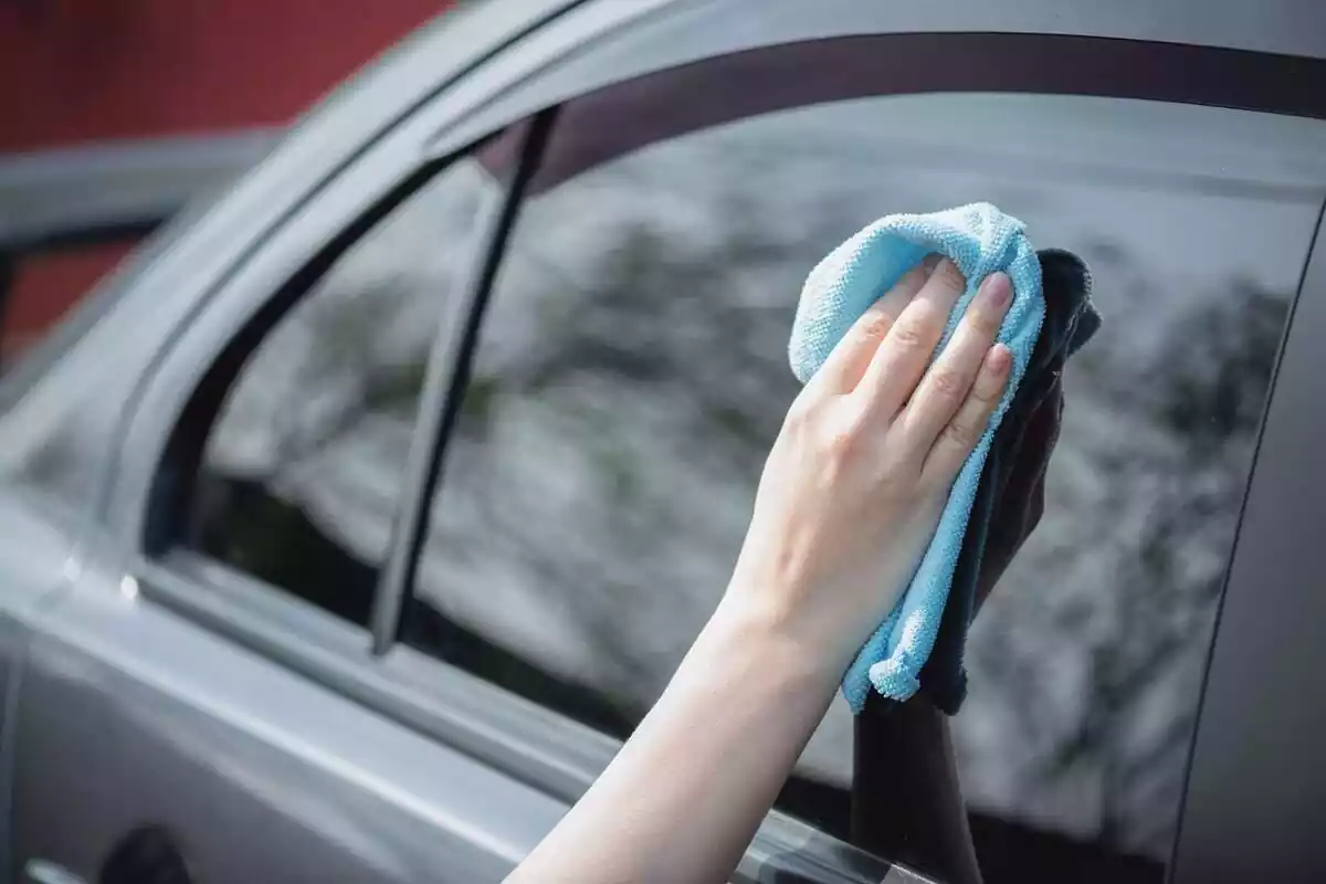 Foto d'una mà netejant la finestra d'un cotxe.