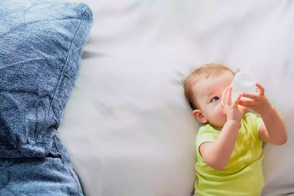 Imatge d'un bebè prenent un biberó a sobre d'un llit