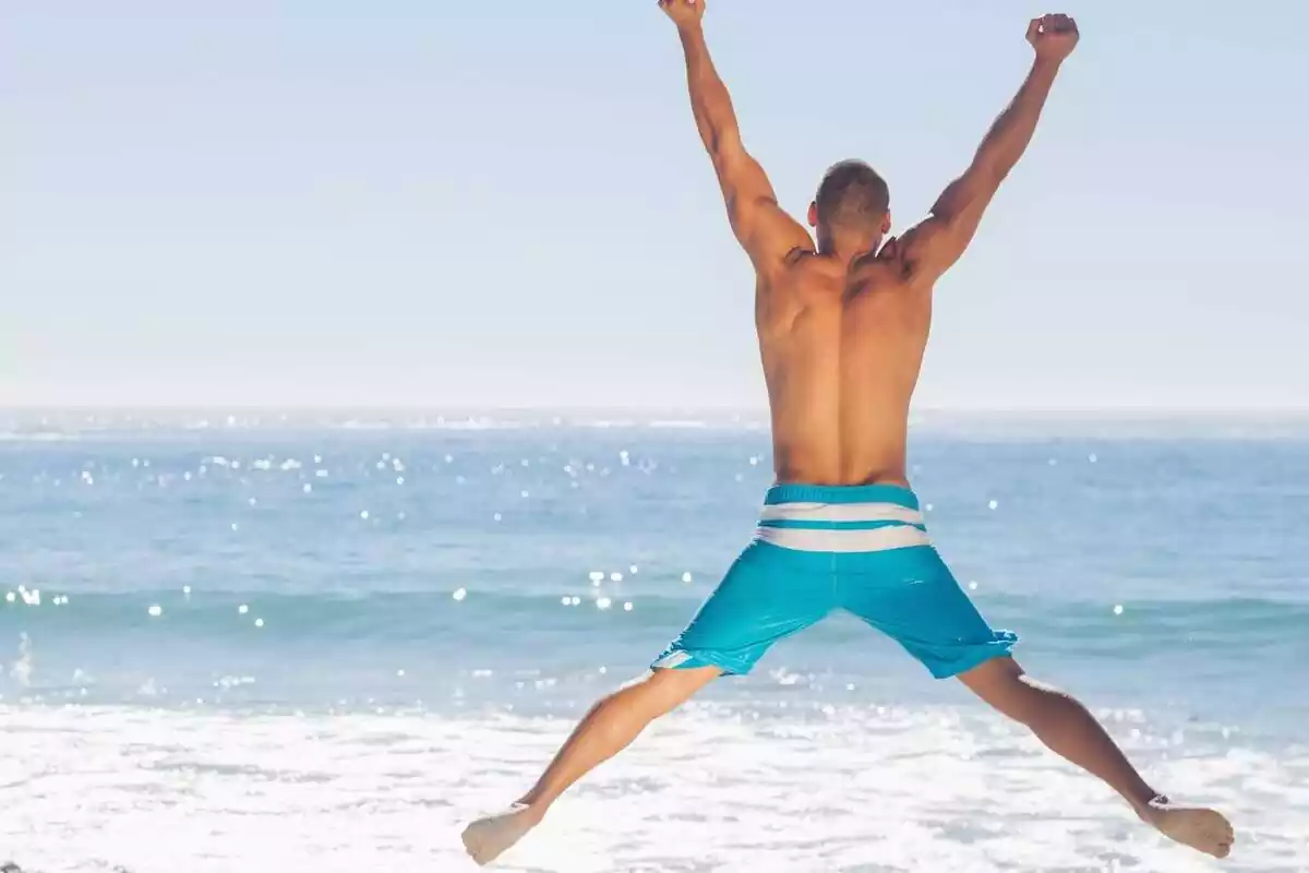 Imatge d'un home d'esquena en banyador saltant a la platja