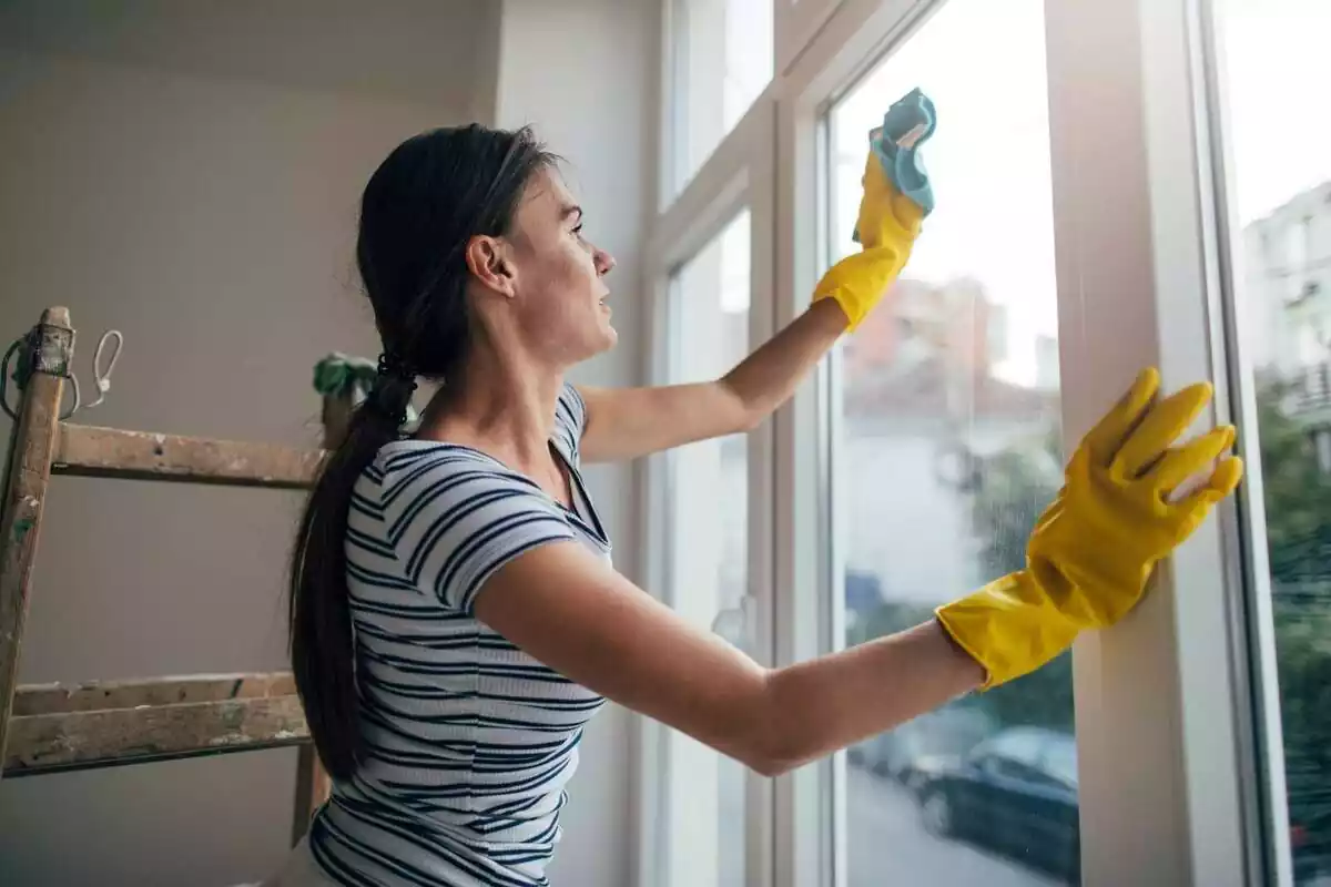 Foto d'una dona netejant un vidre amb una baieta.
