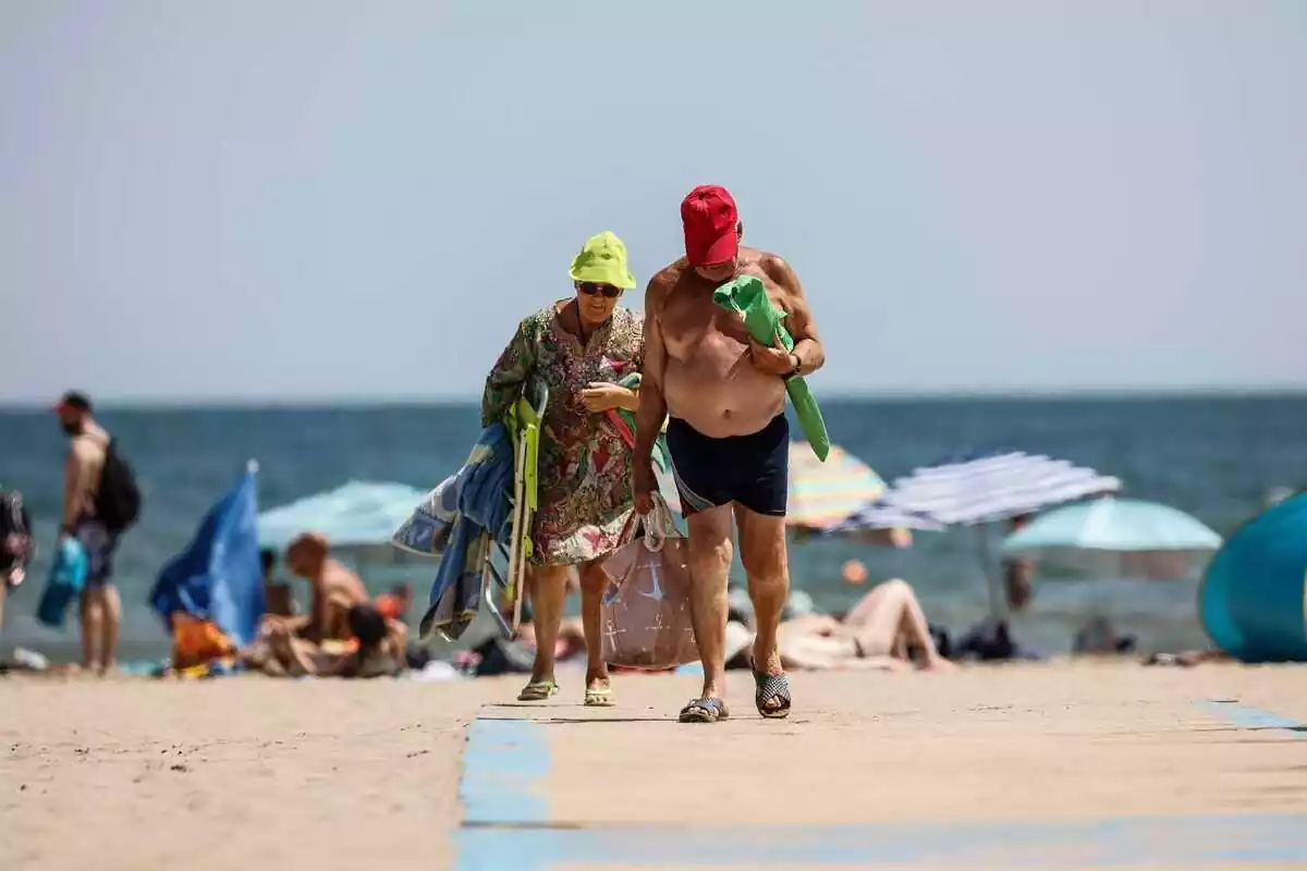 Imatge de dues persones marxant de la platja a València.