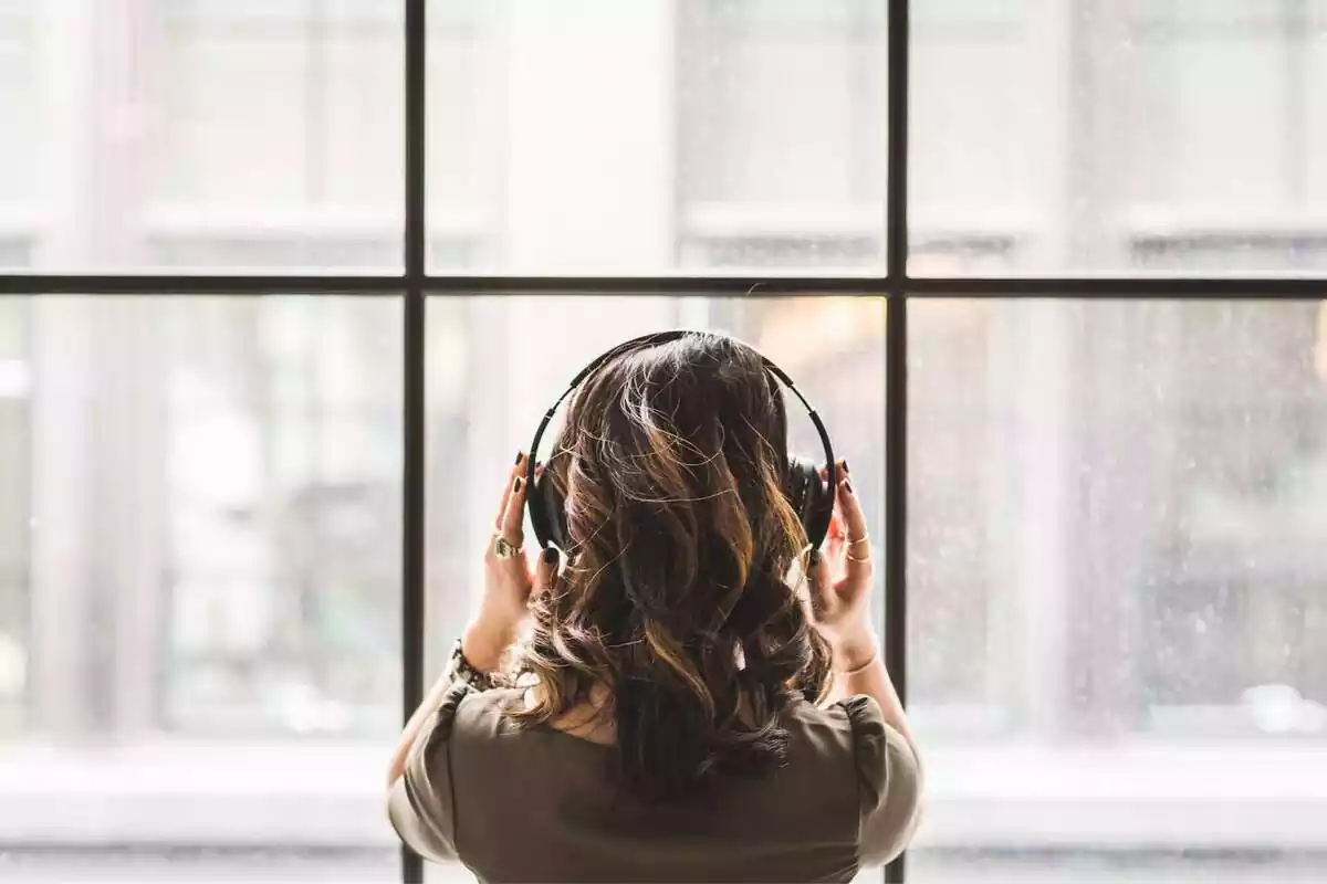 Imatge d'una dona d'esquena mirant per la finestra mentre escolta música amb uns auriculars