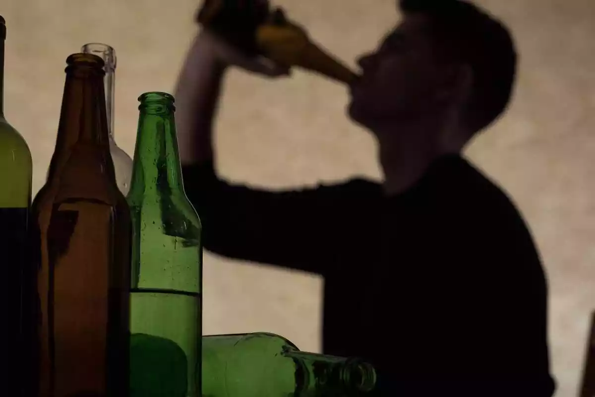Pla desenfocat d'un jove bevent alcohol i diverses ampolles buides