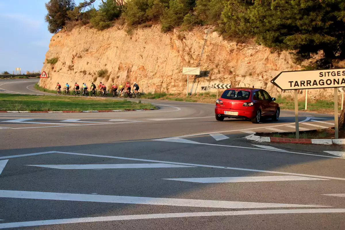 Una desena de ciclistes a la C-31 a les Costes del Garraf amb un cotxe darrera seu