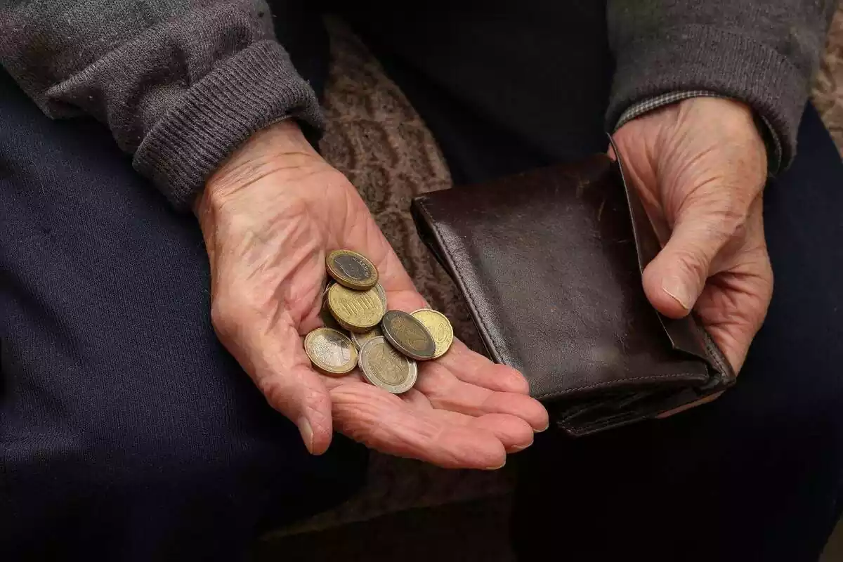 Foto de les mans d'una persona gran amb unes monedes d'euro i una cartera.