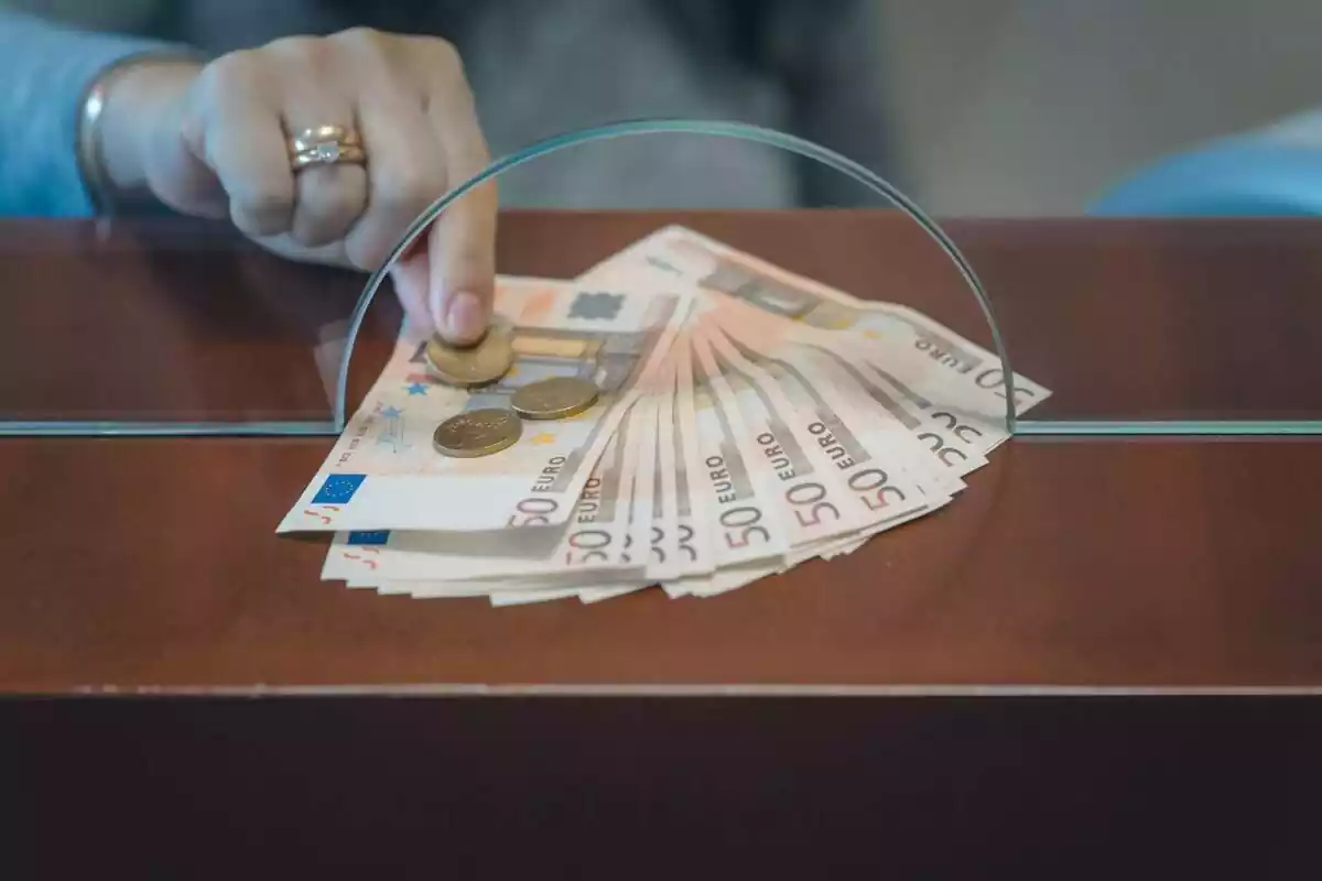Imatge d'una dona recollint diners a través de les finestretes del banc
