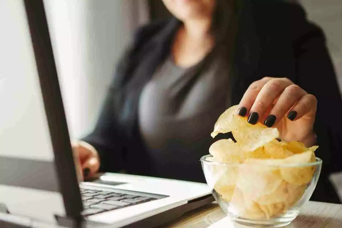 Imatge d'una noia davant d'un ordinador i menjant patates xips