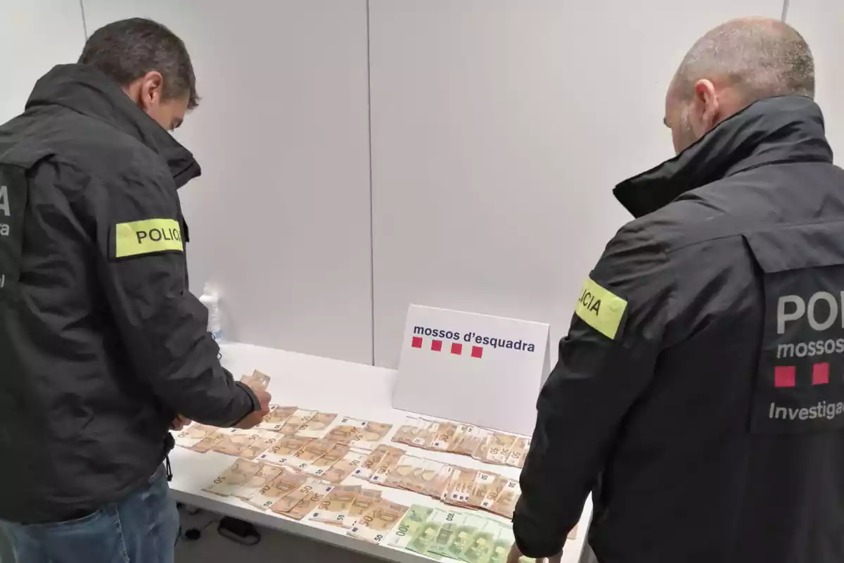 Imatge de dos agents dels Mossos amb diners en efectiu que s'han intervingut a la suposada estafadora