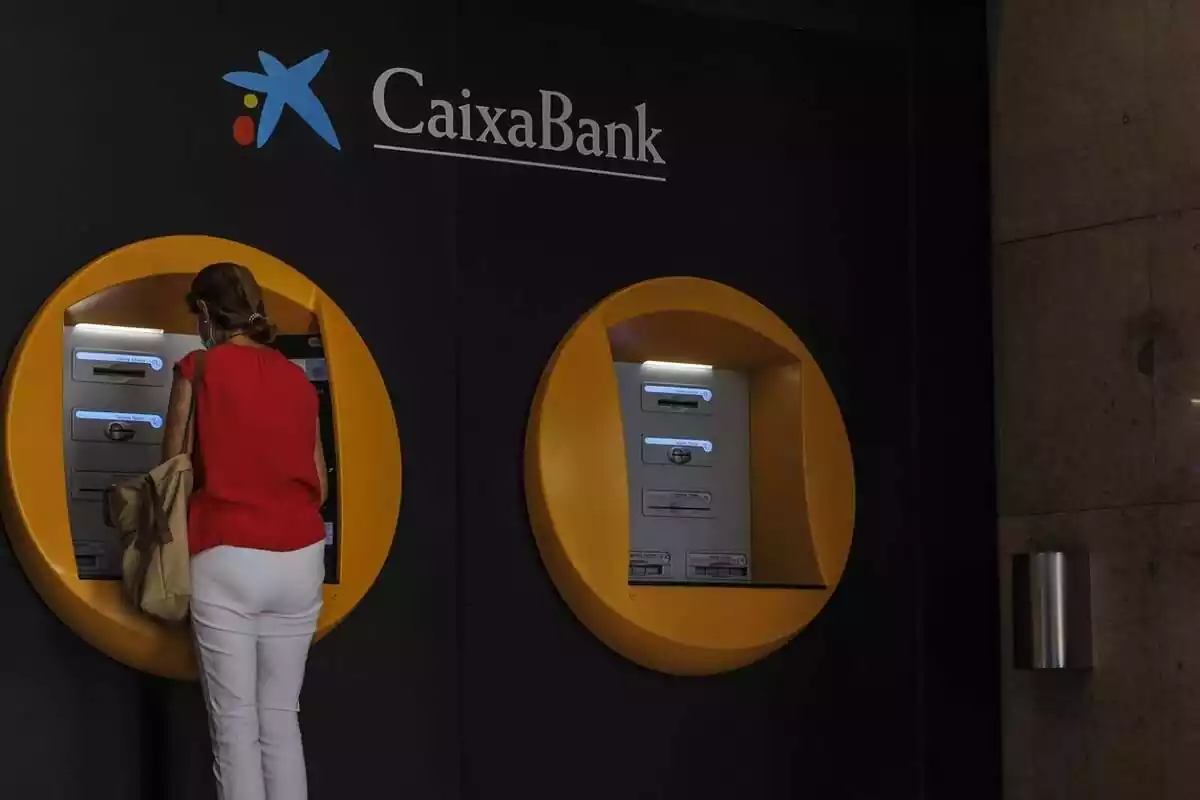 Foto d'una dona traient diners d'un caixer de CaixaBank.