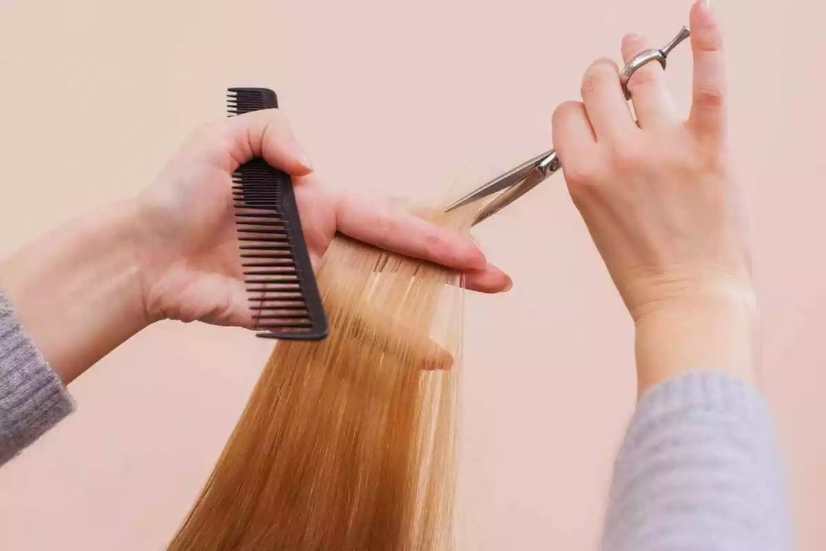Foto d'una persona tallant-li els cabells i pentinant una altra.