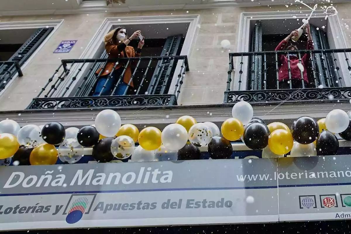 Façana de 'Doña Manolita' amb globus i dues persones celebrant als balcons.