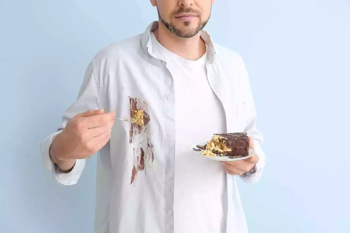 Home amb una camisa blanca tacada i amb un pastís de xocolata a la mà