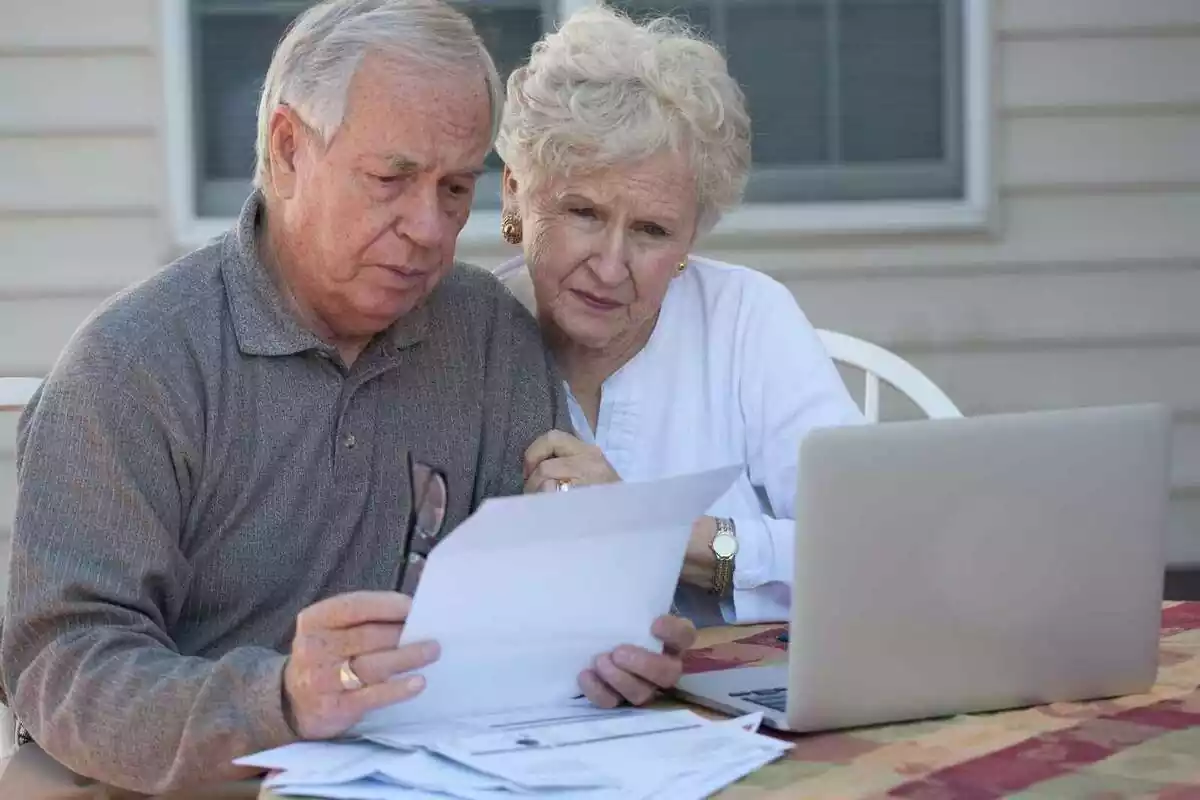 Matrimoni d'ancians mirant un portatil i unes factures