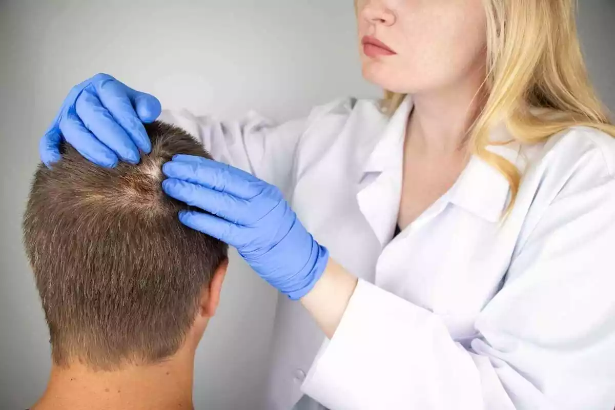 Foto d'una dermatòloga examinant el cabell d'un home.