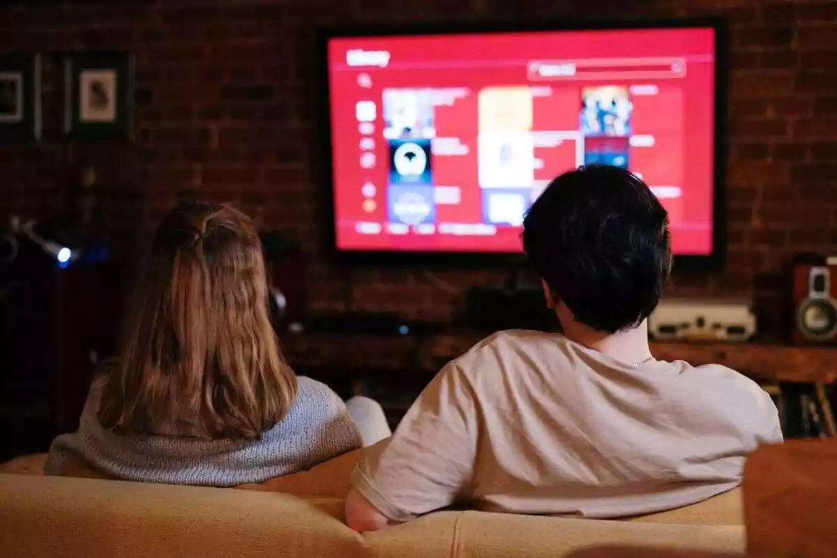 Imatge de dues persones d'esquena assegudes al sofà mirant la televisió