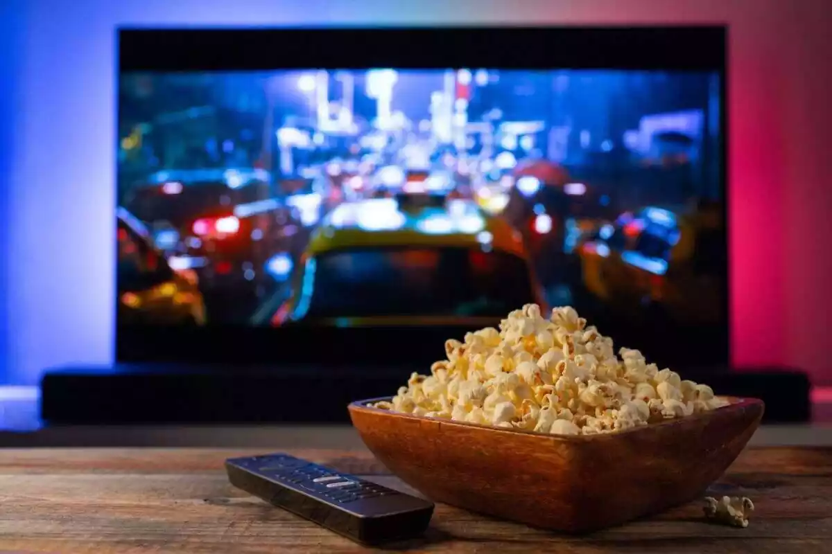 Imatge d'un bol de crispetes sobre una taula i una televisió de fons