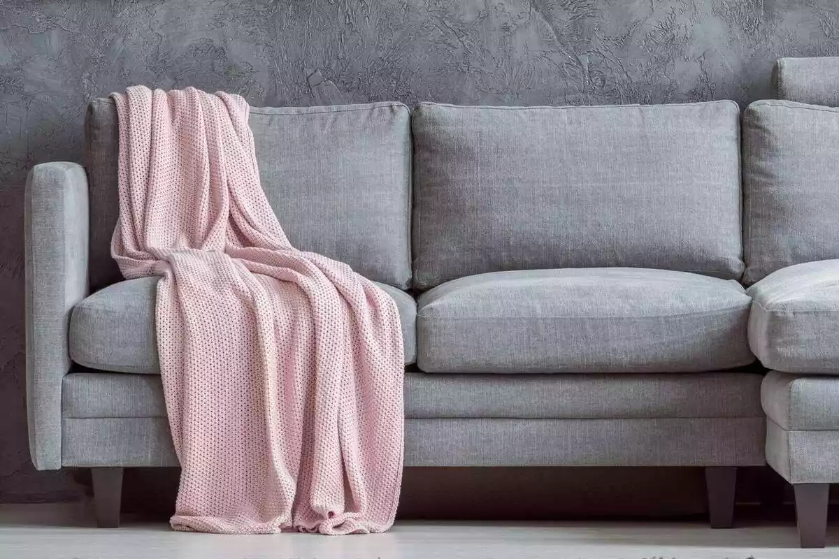 Imatge d'un sofà de tela gris amb una manta de color rosa