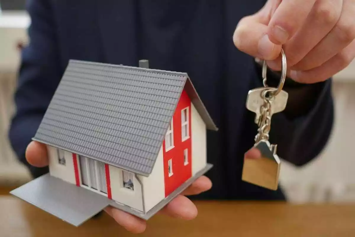 Imatge d'una persona amb una maqueta d'una casa en una mà i amb unes claus a l'altra