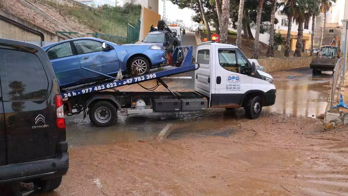 Una grua enduent-se un dels vehicles afectats per la baixada d'aigua de l'Ampolla