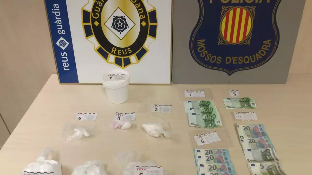 Una taula amb la cocaïna i els bitllets incautats, i els escuts de la Guàrdia Urbana de Reus i els Mossos d'Esquadra