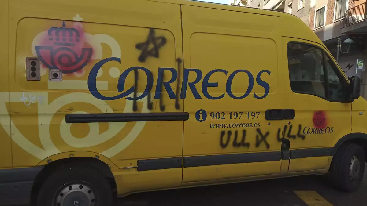 Lateral d'una furgoneta de Correus amb una estelada pintada, els logotips tapats i la frase 'ull per ull' escrita