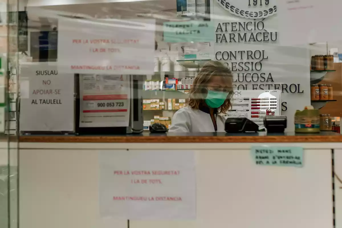 Imatge d'una farmàcia amb una farmacèutica amb mascareta durant l'estat d'alarma pel coronavirus
