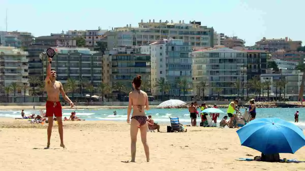 Pla sencer d'un noi i una noia jugant a les pales a la platja de Salou, amb diverses persones prenent el sol el 29 de maig del 2020.