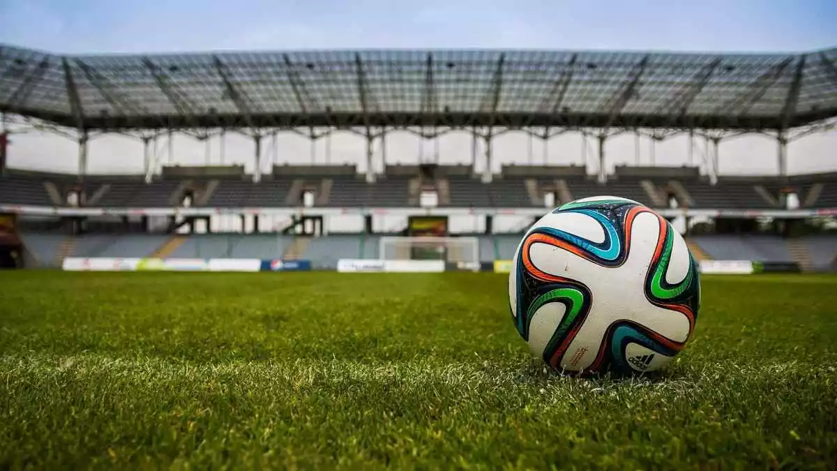 Imatge d'una pilota de futbol sobre la gespa amb les graderies de l'estadi buides