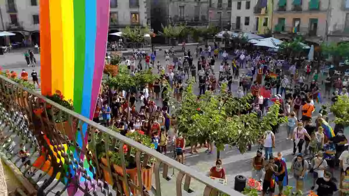 Pla general de la plaça Major de Prades plena de persones concentrades contra l'homofòbia, amb la bandera LGTBI penjada en primer terme a l'Ajuntament. Imatge del 30 de juliol del 2020.