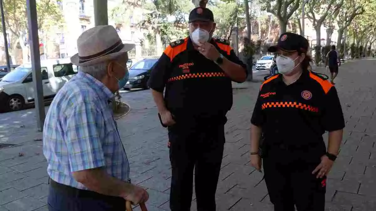 Pla mitjà de dos voluntaris de Protecció Civil de Reus parlant amb un veí al passeig Sunyer