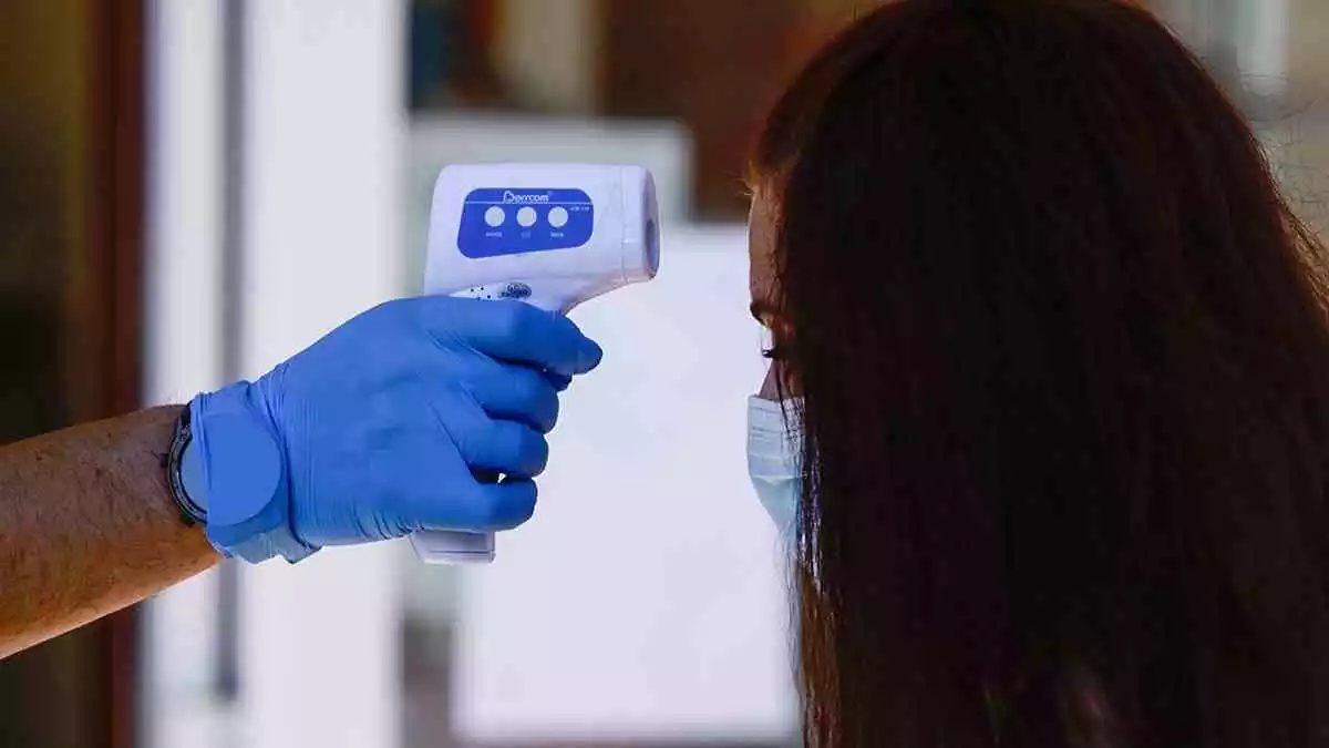 Un professional sanitari pren la temperatura a una dona abans de realitzar la prova PCR