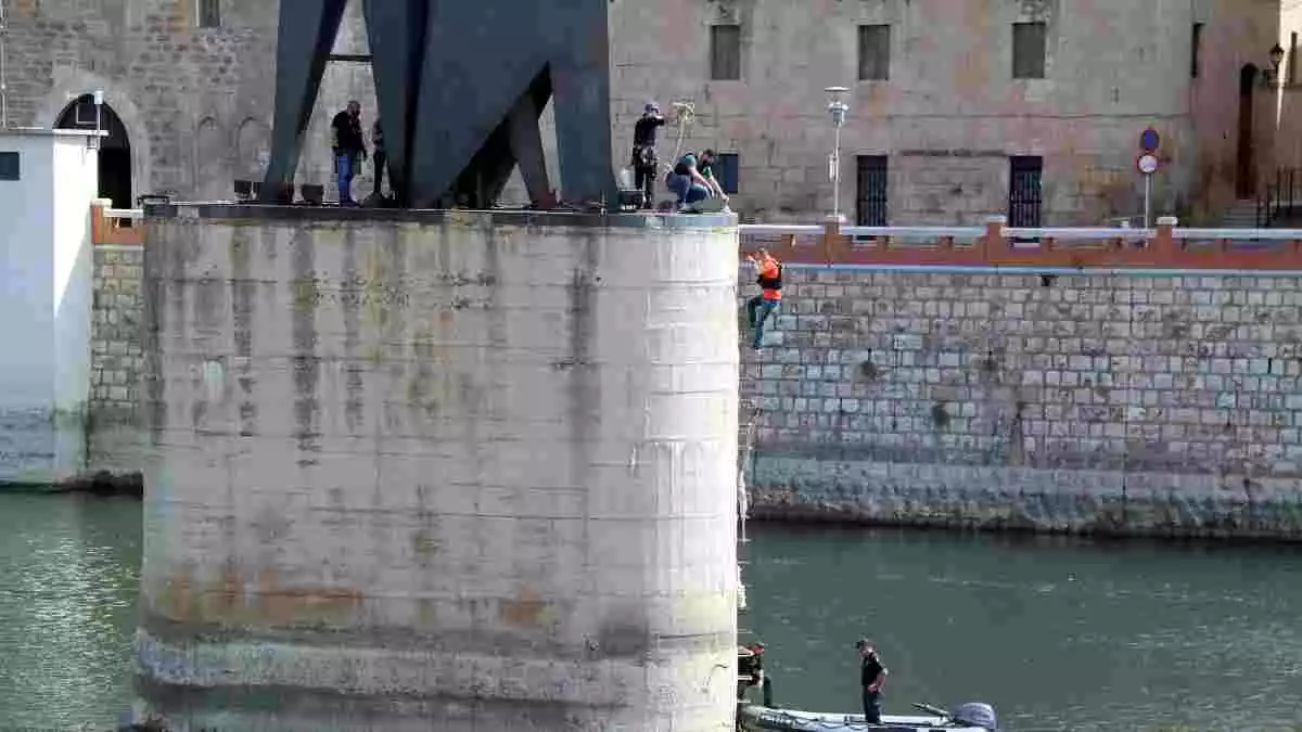 Pla general de la pilastra del monument franquista de l'Ebre de Tortosa amb els agents dels Mossos fent una inspecció ocular mentre un d'ells es despenja cap a l'embarcació.