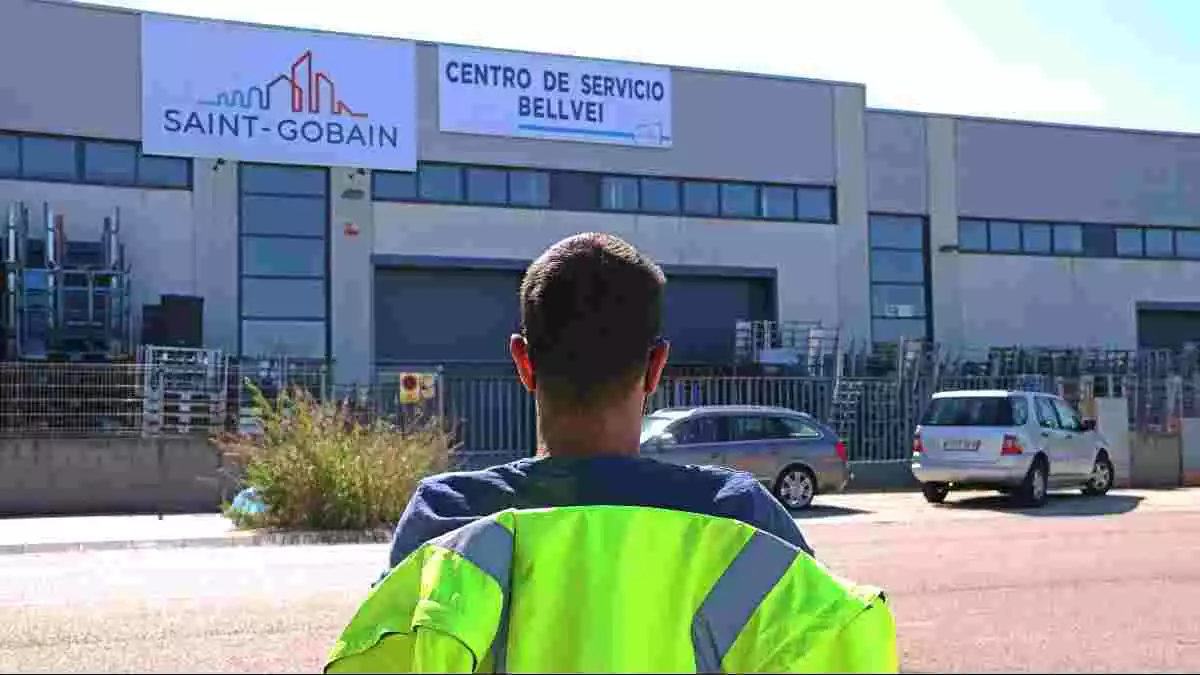Pla obert d'un treballador de Saint-Gobain d'esquenes i assegut davant del centre logístic de l'empresa al polígon de Bellvei, on la plantilla bloqueja el magatzem
