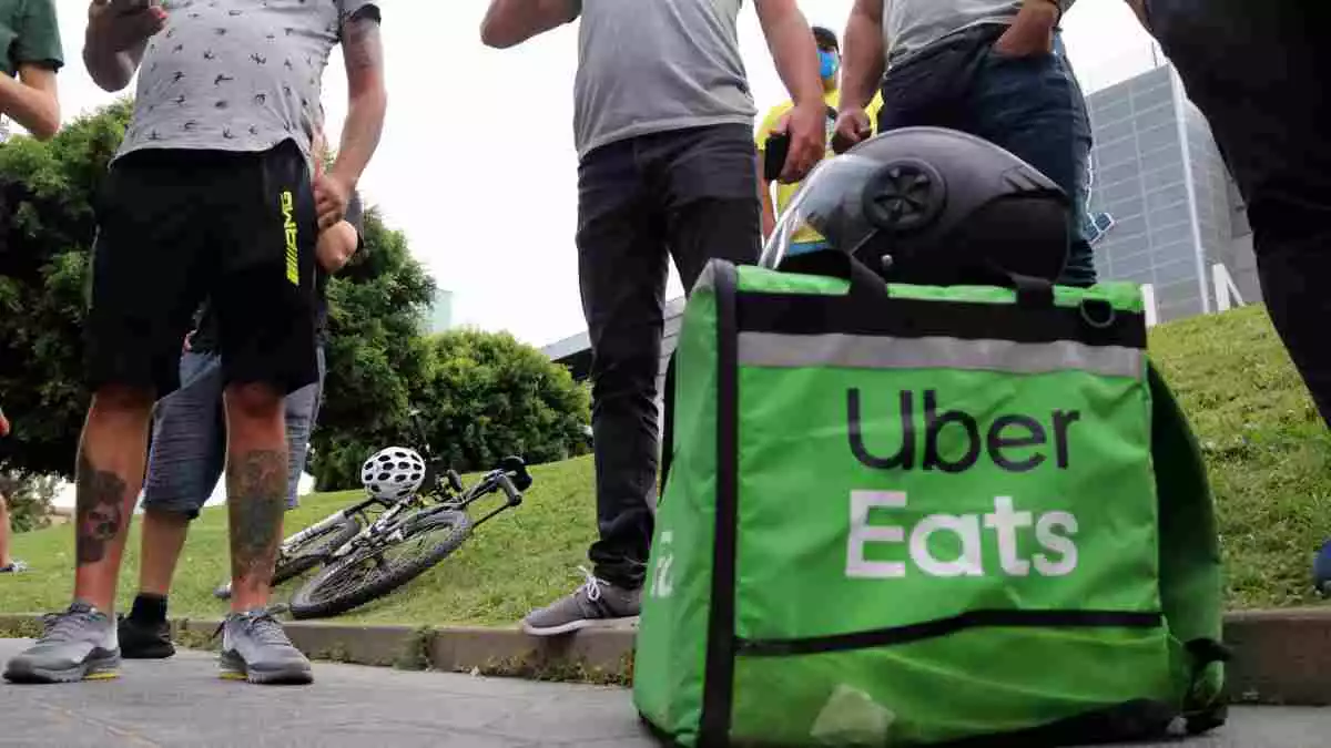 Una motxilla d'Uber Eats a terra, a Tarragona, amb diversos riders al seu voltant.